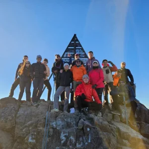 Tourists standing beside the iconic metal pyramid at the summit of jebel toubkal trek Tourists standing beside the iconic metal pyramid at the summit of jebel toubkal trek