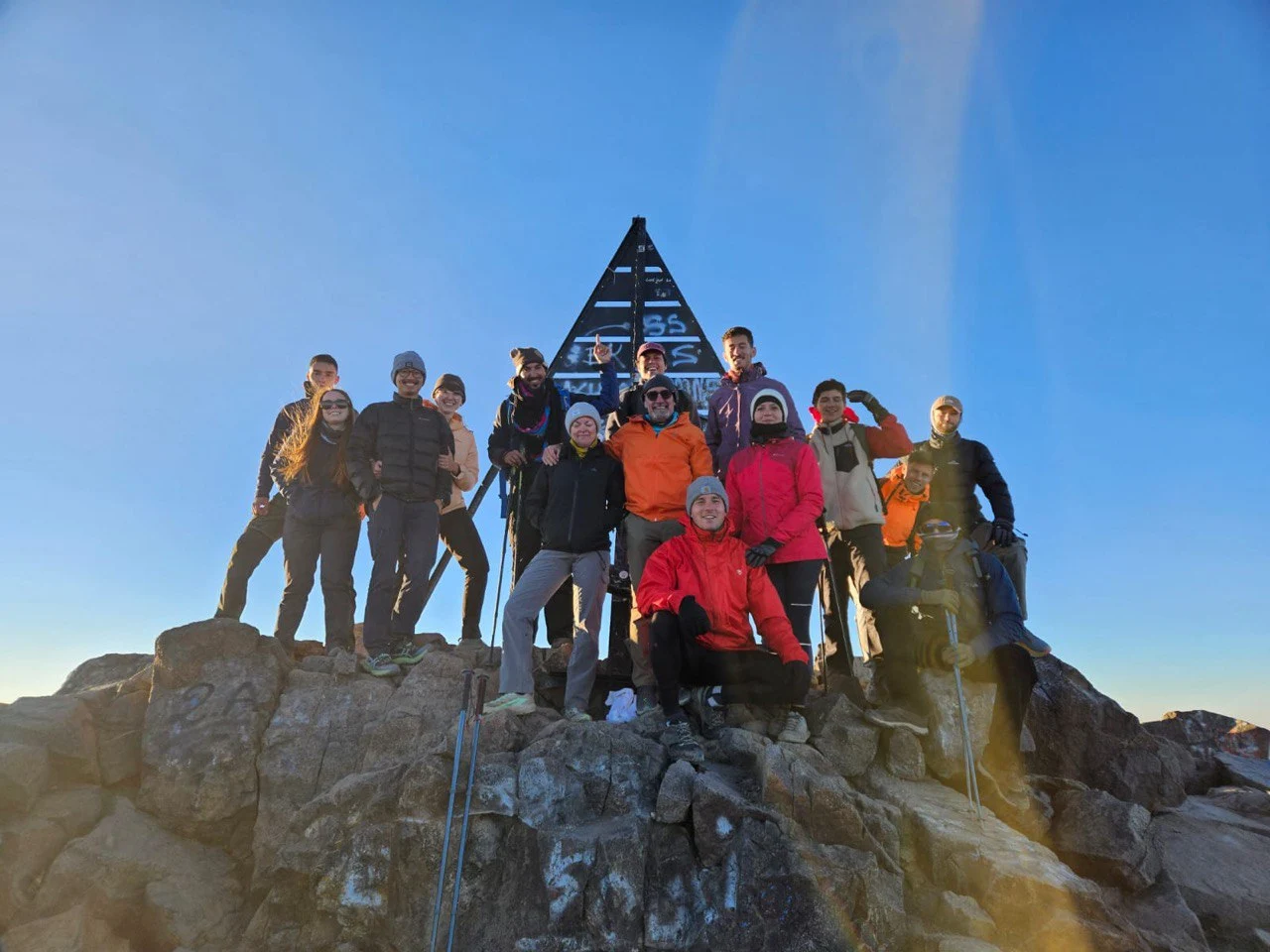 Tourists standing beside the iconic metal pyramid at the summit of jebel toubkal trek